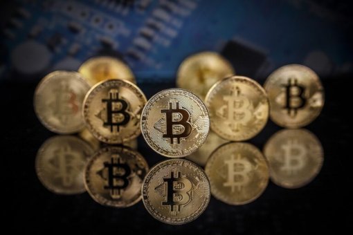 Несколько золотых биткойнов на отражающей поверхности с одним биткойном в фокусе